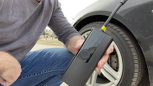 A compact cordless tire inflator being used on a vehicle tire